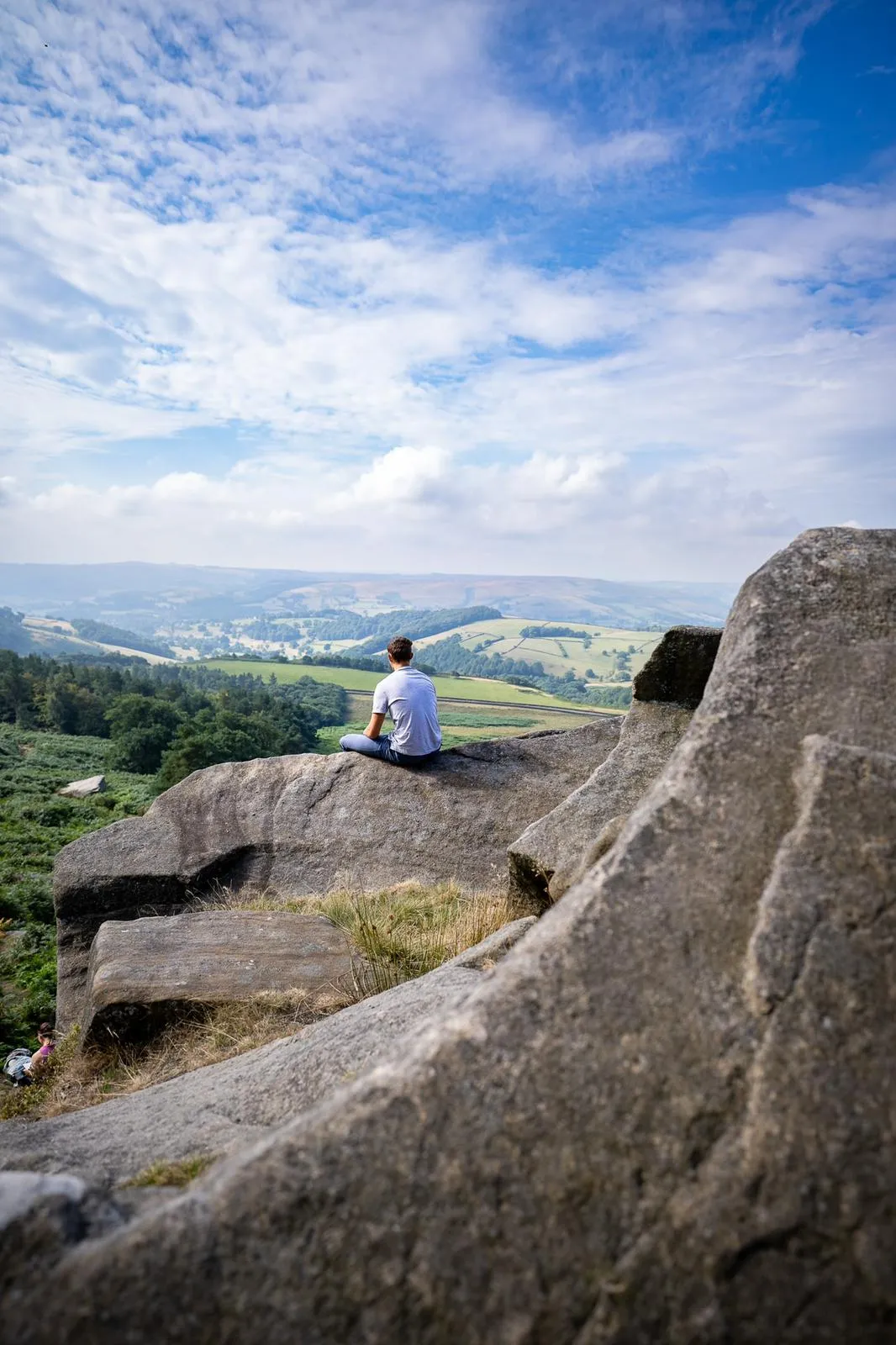 Hayden is sat on top of a boulder, looking over the Peak District